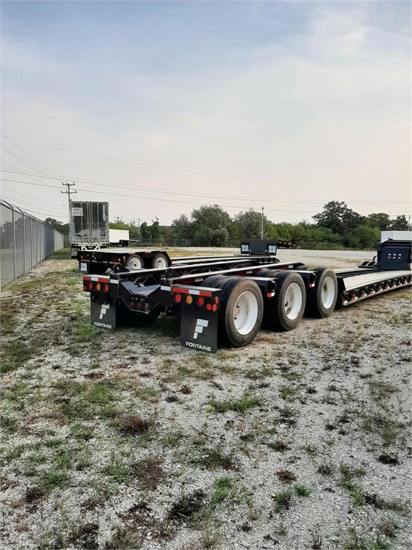 Fontaine 55 ton lowboy trailer with multiple axles and flat deck, rear view showing mud flaps with Fontaine logo and stacked tires.