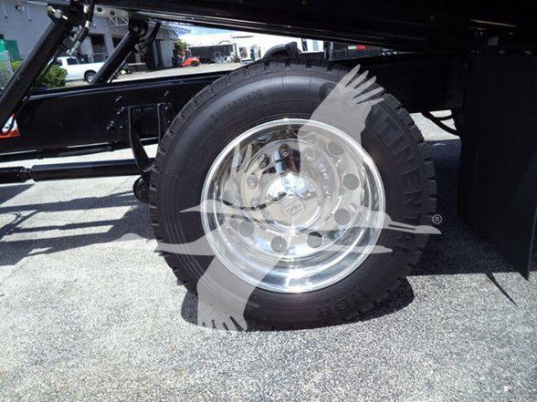 Wheel and tire assembly of a new International MV tow truck showing a polished chrome rim and heavy-duty tire under the chassis.