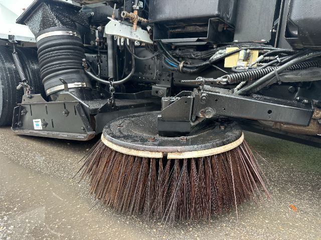 Isuzu NPR-HD sweeper front undercarriage with circular street broom and hydraulic components visible.