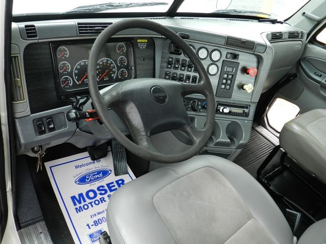 Cab interior of a Freightliner truck showing steering wheel, dashboard with gauges, and control panel.