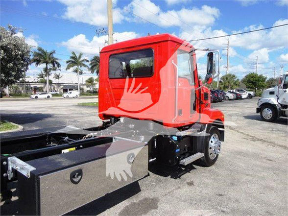 Red Mack MD6 cab and chassis in a dealership lot, side view showing the cab with black chassis and storage compartments.