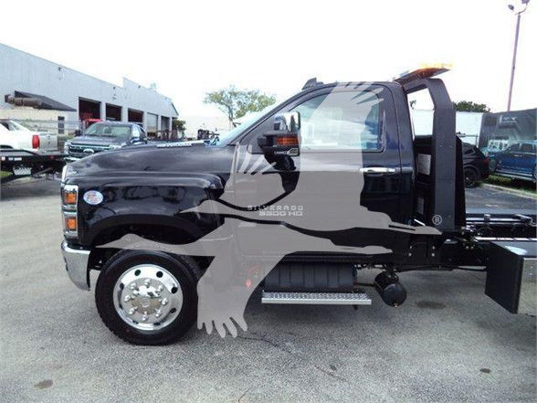 Truck cab side view of a 2023 Chevrolet Silverado 6500HD tow truck with lifted wheel, flatbed, and step side; visible chrome wheel, side steps, and towing apparatus.