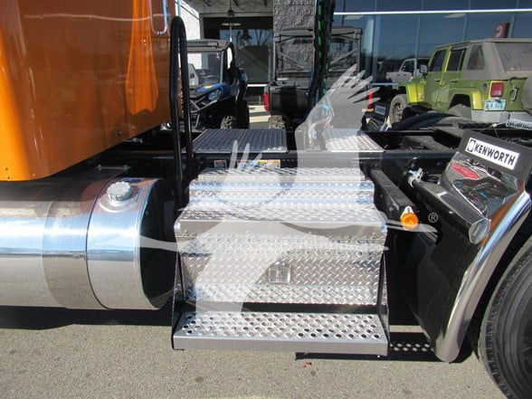 Kenworth W900L truck chassis side view with metal diamond plate step and fuel tank, visible Kenworth logo on adjacent parts.