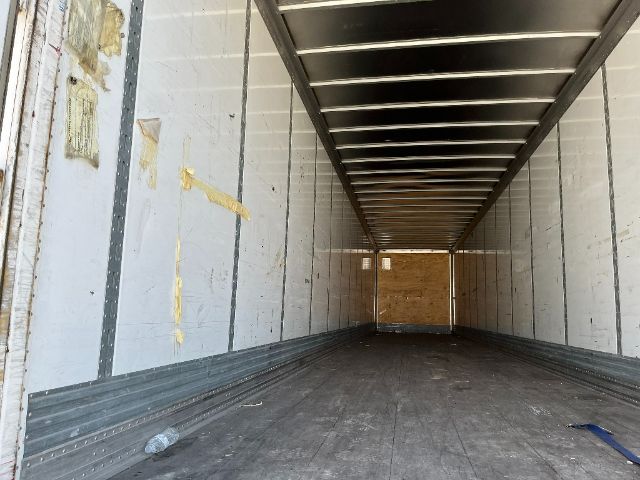 Interior of a cargo trailer with metal walls and ribbed ceiling, empty long trailer with plywood at far end.
