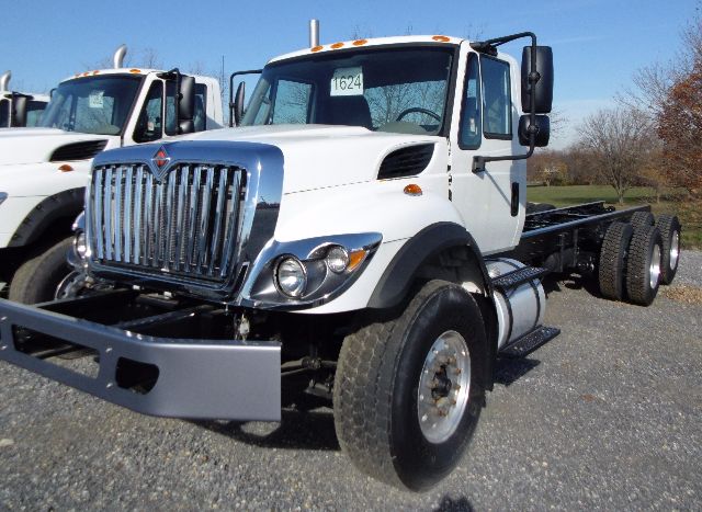 Truck chassis with white cab and grille showing International emblem, side view of front wheels, hood scoops, and dual rear axles.