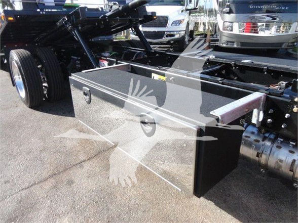 Truck chassis with a metal tool/storage box mounted under the frame near the rear wheel area; chevron pattern watermark overlay visible on the box.