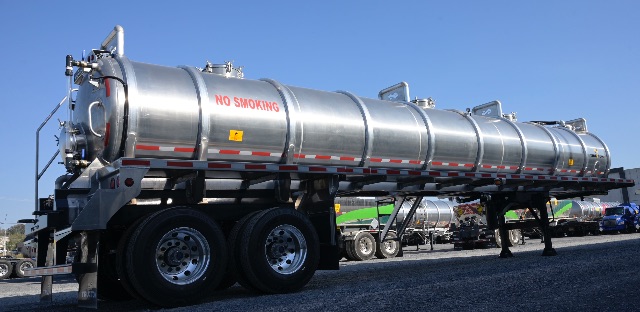 Aluminum vacuum trailer with a long cylindrical tank mounted on a multi-axle trailer. Red 'NO SMOKING' text on side, various safety decals and reflective tape along the tank.