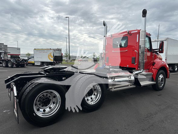 2026 Kenworth T880 tractor with red cab and chrome exhaust stacks, side steps, and dual rear axles visible in a truck lot.