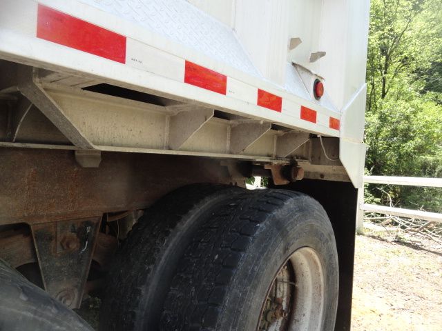 Trailer dump bed with dual rear wheels and reflective red/white side rails; view under carriage showing frame, suspension, and tire.