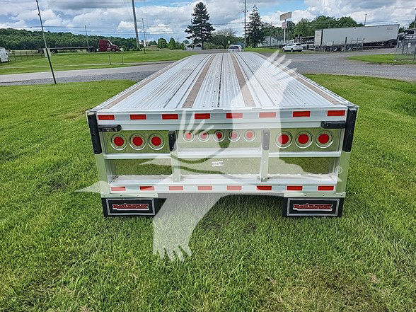 Flatbed trailer rear view with multiple circular taillights, reflective tape, and aluminum deck.