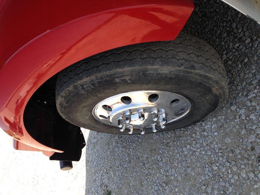 Wheel of a red Kenworth T800 truck showing chrome dual wheel hub with lug nuts and part of front fender.