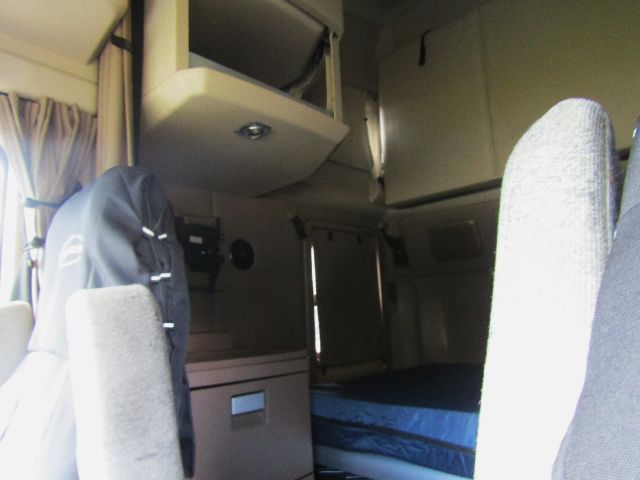 Kenworth T680 cab interior showing driver's seat, sleeping area with blue mattress, overhead storage cabinets, and dashboard components.