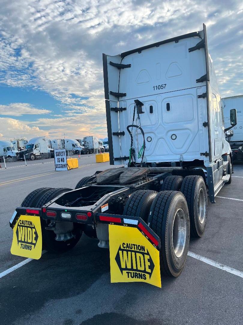 Freightliner Cascadia 126 semi-truck rear view showing dual rear axles and fifth-wheel area with yellow caution wide turns mudflaps.