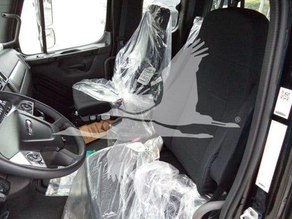 Interior of a new Freightliner Business Class M2 106 truck cab with plastic seat covers and steering wheel, driver door open.