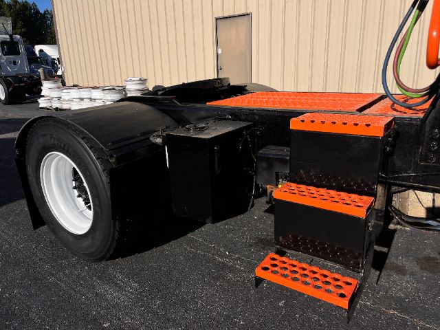 Tractor-trailer chassis with black and orange steps, large rear wheel, and side platform; visible exhaust and toolbox area near the cab.