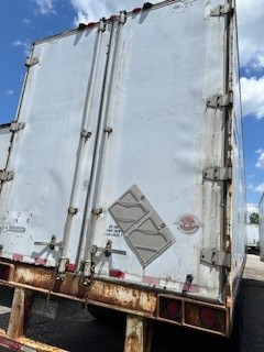 Rear view of a used Great Dane dry van trailer with white doors, rust on the lower frame, corner hinges, and a diamond-shaped safety placard on the door.