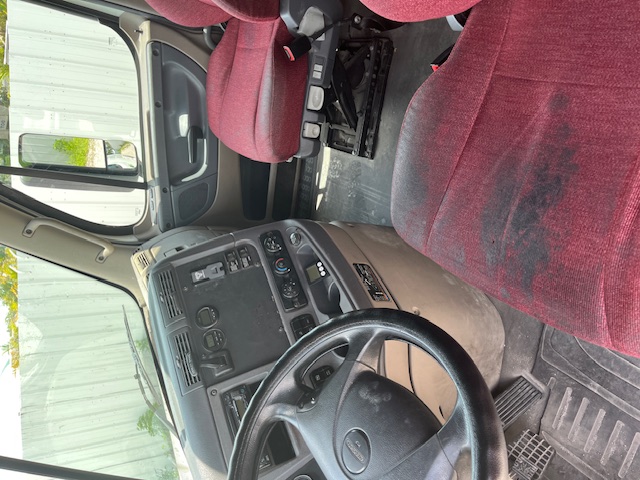 Cab interior of a 2016 Freightliner Cascadia with red driver and passenger seats, steering wheel, dashboard, and central control area.
