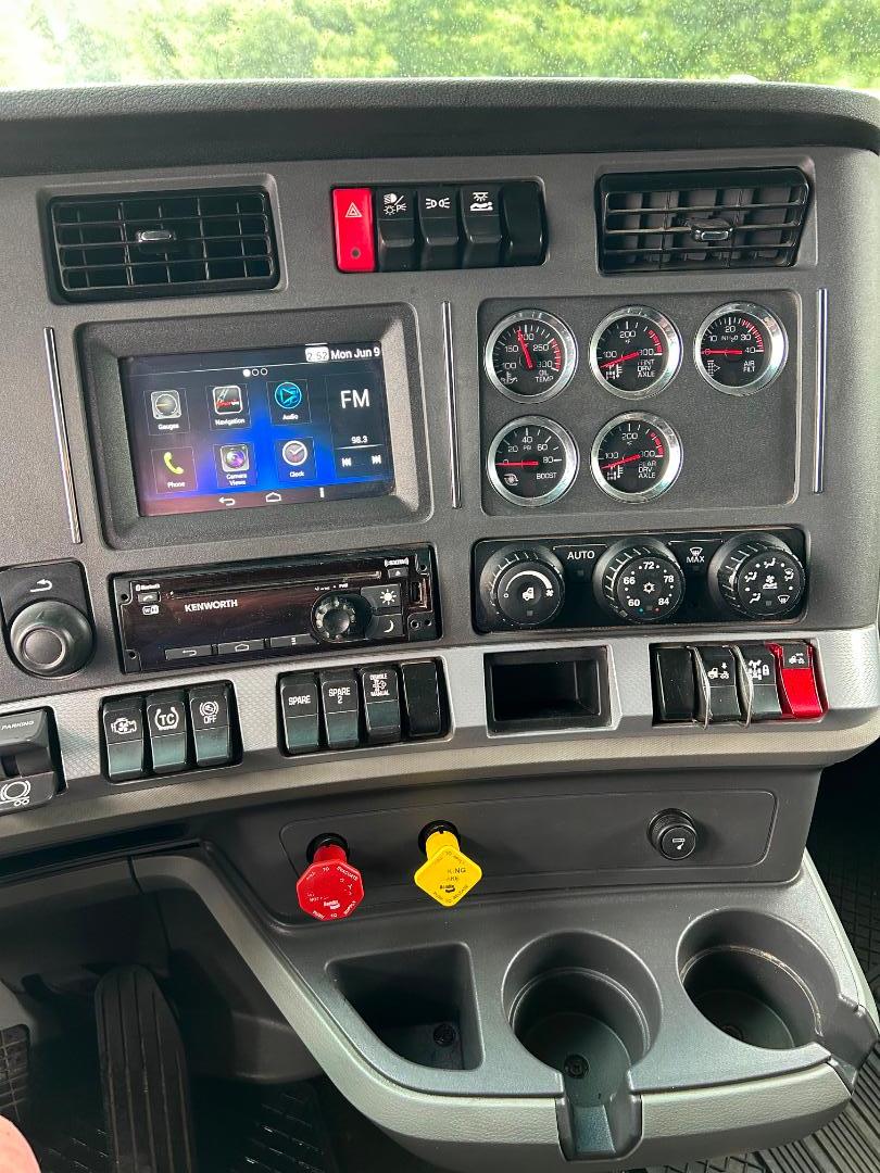 Kenworth T680 dashboard and center console with touch screen infotainment, multiple gauges, climate controls, switches, and red/yellow controls.