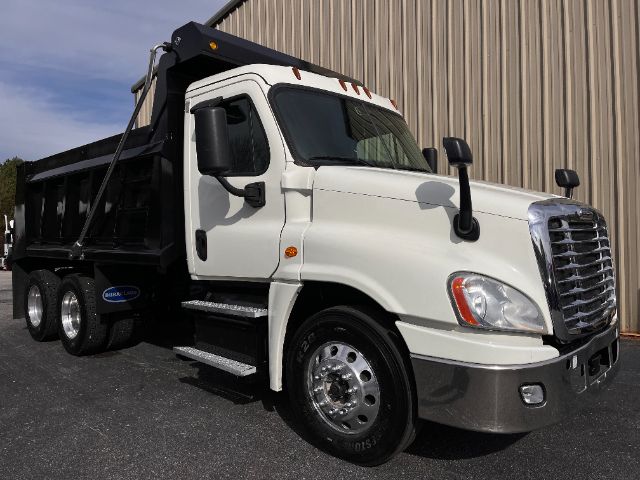 Dump truck front and side view showing white cab and black dump bed, Freightliner logo on grille, large side mirrors, aluminum wheels, step ladder.