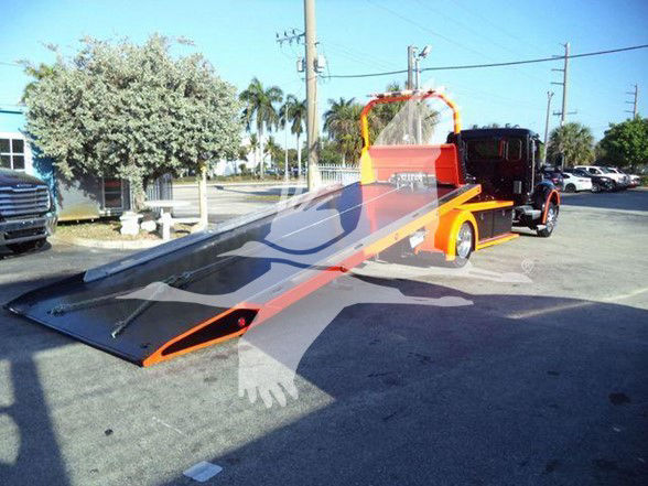 Tow truck with a flatbed ramp extended, black cab, orange bed and yellow rails; no visible labels on the truck body.