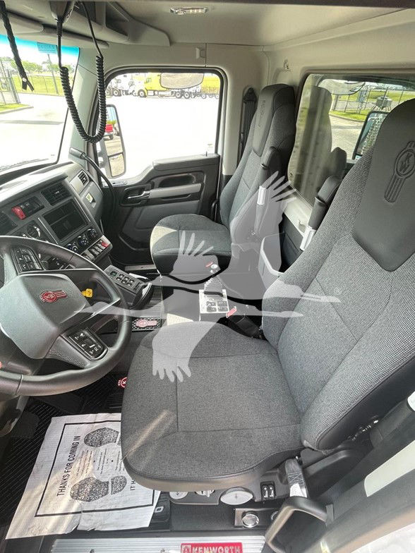 Kenworth T880 truck cab interior showing driver and passenger seats, steering wheel with Kenworth emblem, center console, and dashboard controls.
