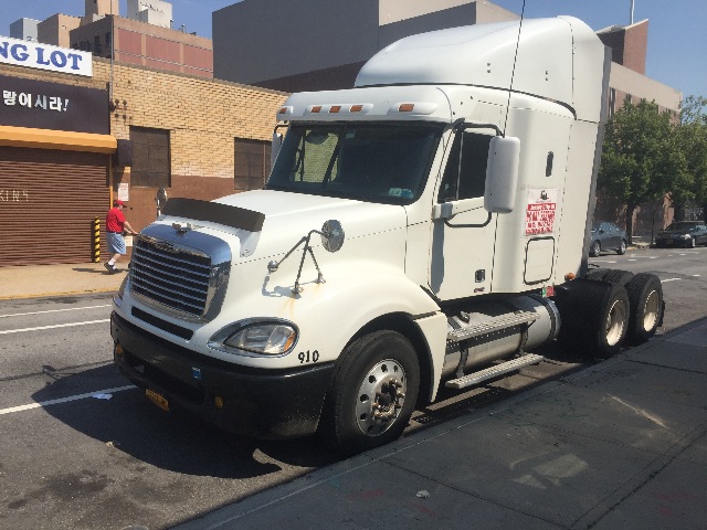 Freightliner Columbia conventional sleeper tractor truck, white, with aerodynamic sleeper cab and triple rear axles on street.