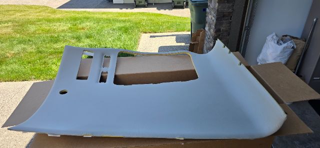 Light gray truck interior panel/hood piece with cutouts and vent openings resting on cardboard in driveway.