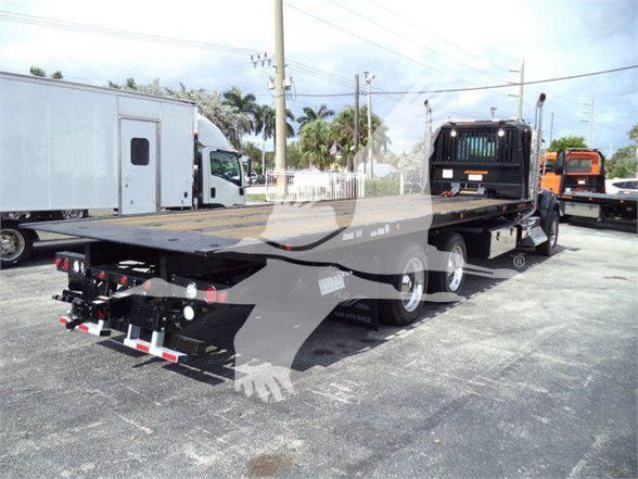 Kenworth T880 flatbed tow truck in a lot with trailers in background.