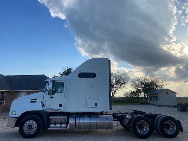 Truck side view showing 2015 Mack CXU613 sleeper cab with fuel tanks and dual rear axles.