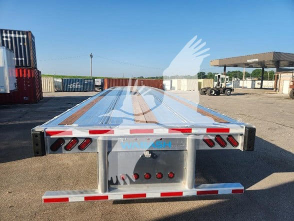 Flatbed trailer from rear showing Wabash branding and taillights, with reflective red-and-white stripes and loading area.