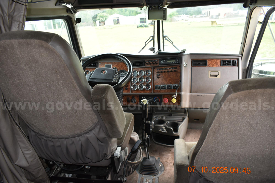 Cab and Chassis interior of a 2003 Kenworth W900 showing brown dashboard, multiple round gauges, steering wheel, gear shifter, and center console.