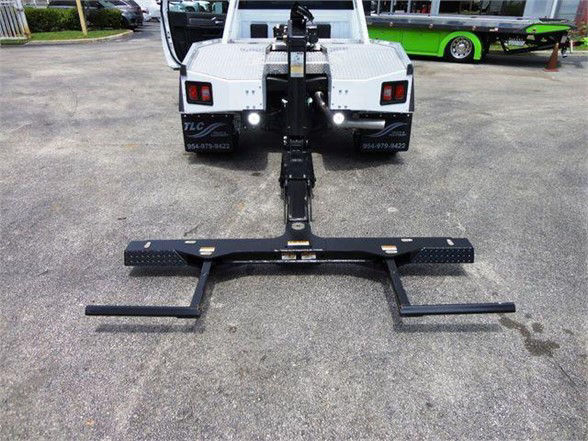 Front view of a white Ram 4500 SLT tow truck with a heavy-duty hitch setup attached to the rear, showing a horizontal receiver bar and stabilizing legs.