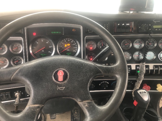 Kenworth T800 cabin steering wheel and dashboard with multiple gauges and a gear shifter visible.