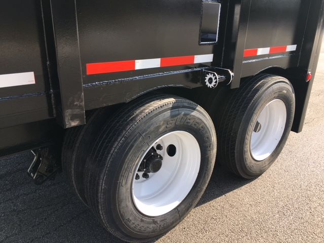 Dual-axle dump trailer with black body and white wheels; visible tires labeled Super Traction; red and white reflective strips along the side.