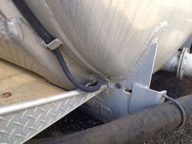 Truck part showing a large cylindrical vacuum tank with welded metal bracket and a black protective conduit, side view highlighting mounting area and a large hose.