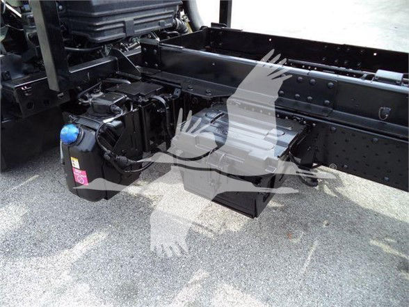 Isuzu NRR chassis area showing a blue-capped reservoir and electrical components mounted near the frame rail.