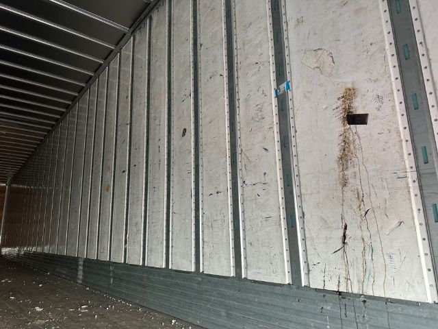 Trailer interior wall panels with vertical support pillars and wear marks; sideload door area visible in a long enclosed trailer.