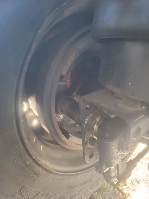 Wheel hub and suspension area of a utility trailer showing a tire, leaf spring, and mounting hardware.