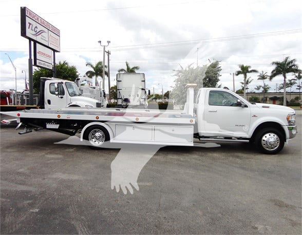 2023 Ram 5500 HD SLT tow truck with flatbed and chrome wheels, side profile view in lot.