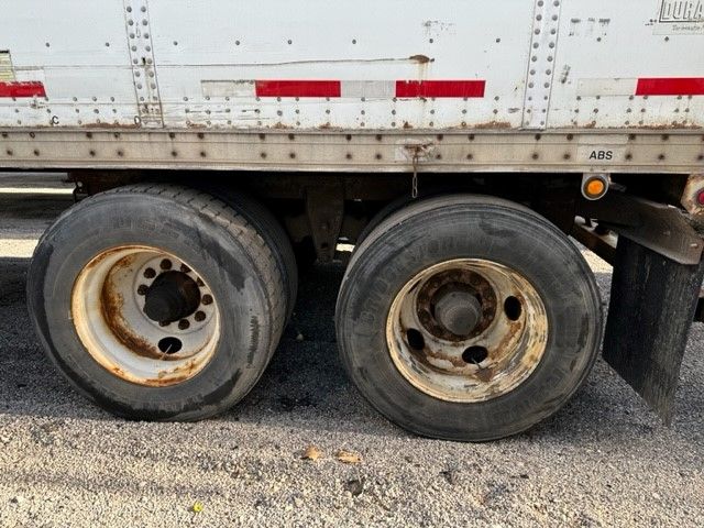 Two rear trailer wheels with rusted rims and wear showing on the tires under a white Wabash Duraplate trailer.