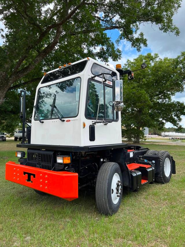 White quad-axle yard truck with orange front bumper and black chassis, Tico Prospotter cab windows, chrome mirrors, and large white wheels parked on grass.