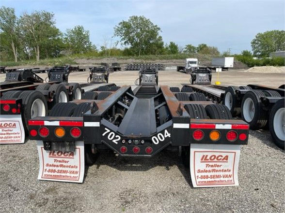 Tractor-trailer lowboy trailer rear view showing dual tandem axles, mud flaps, and rear lights with numbers 702 and 004 on the beam.