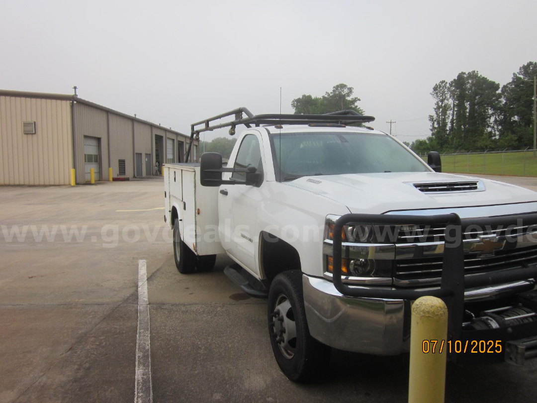 Service body Chevrolet Silverado 3500HD white pickup with front grille guard and utility rack in a parking lot.