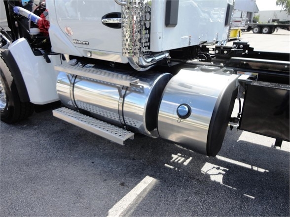 Kenworth W990 truck side showing polished cylindrical fuel tanks, chrome steps, and part of the cab with 'W990' badge.
