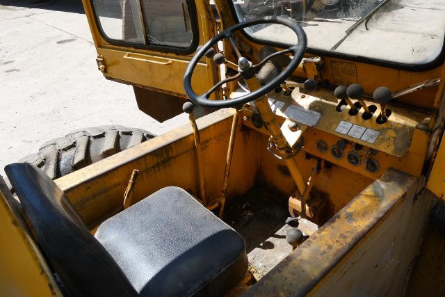Cab interior of a yellow Grove RT58 crane showing steering wheel, control levers, and instrument panel; rugged seat and worn metal framework.