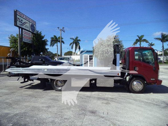 Isuzu NPR XD tow truck with flatbed, side view showing cab and bed, dealership lot in background.