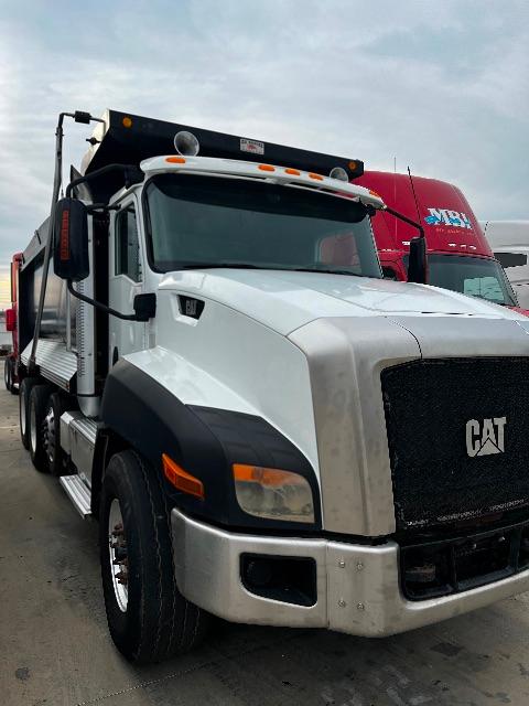 Front-left view of a white Caterpillar T660S dump truck with a red cab in the background, spare tire mounted above the hood, and side steps visible.