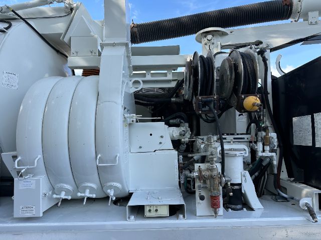 Industrial vacuum truck engine bay showing large reel hoses, hydraulic components, and pump assembly.