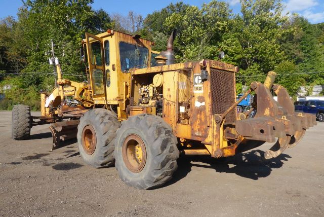 Professional wheeled motor grader with faded Caterpillar branding and visible front blade, orange in color, parked on a dirt lot with trees in background.