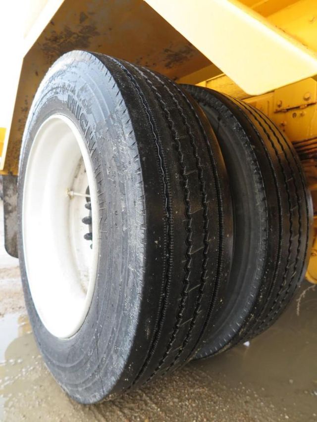 Wheel assembly with heavy-duty dual tires mounted on white rims under a yellow vehicle frame.